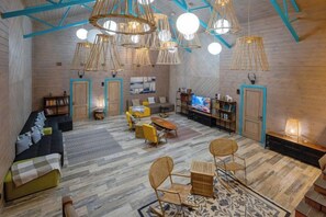 A spacious loft with a high ceiling, exposed wooden beams, and a mix of seating areas including a sofa, chairs, and a small table.