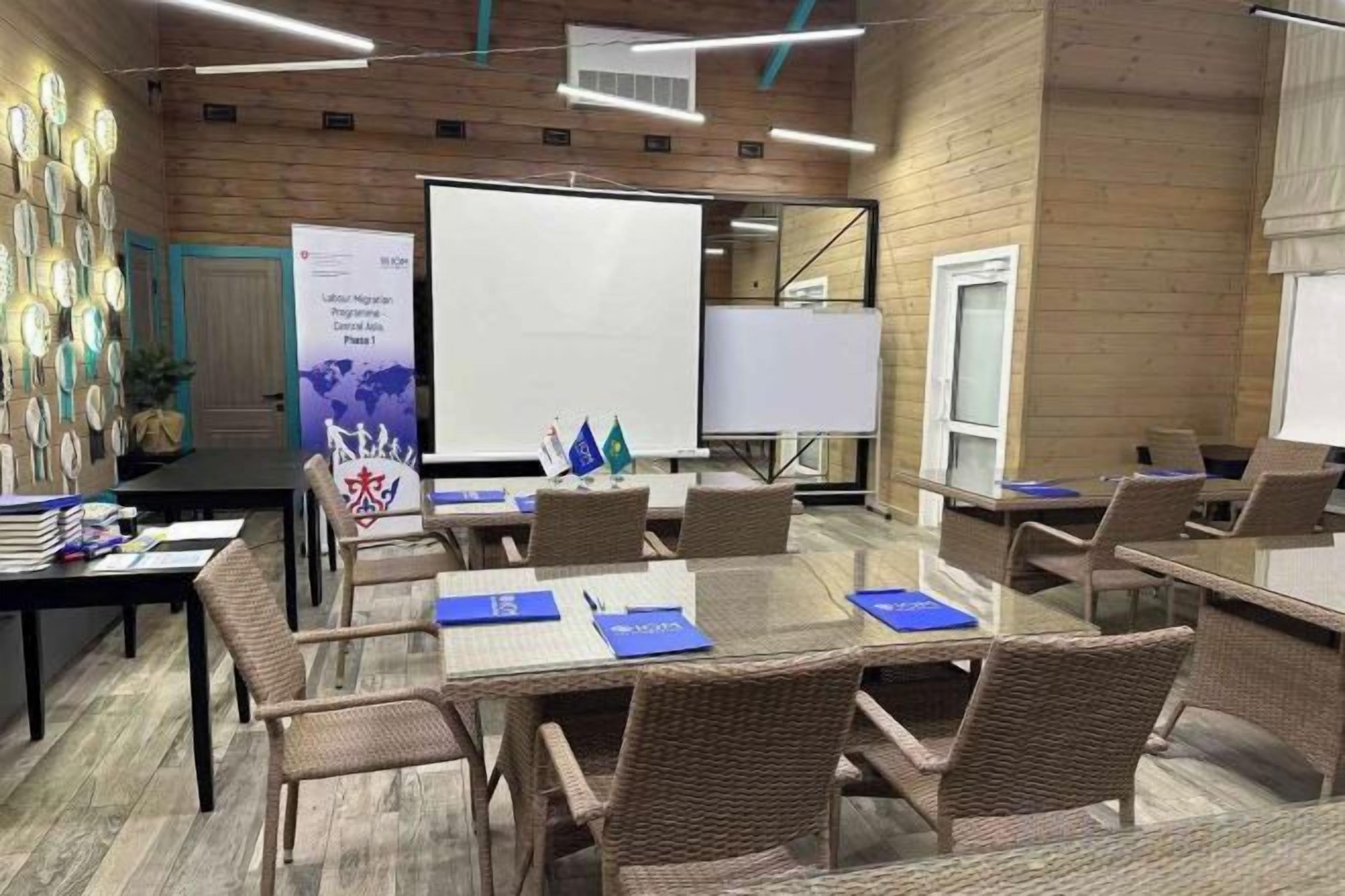 Une salle de conférence équipée d’une grande table, de chaises, d’un tableau blanc et d’un écran de présentation.