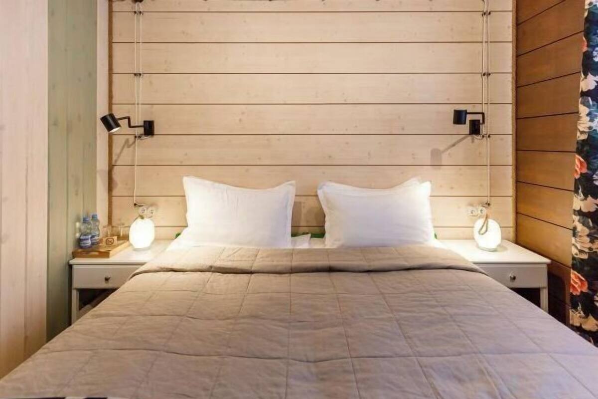 Een bed met een beige sprei, twee witte kussens en bedlampjes.