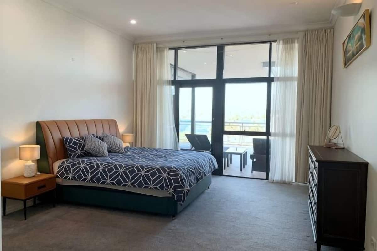 Une chambre d’hôtel avec un lit, des lampes de chevet, une commode et une vue sur l’extérieur grâce à une grande fenêtre.