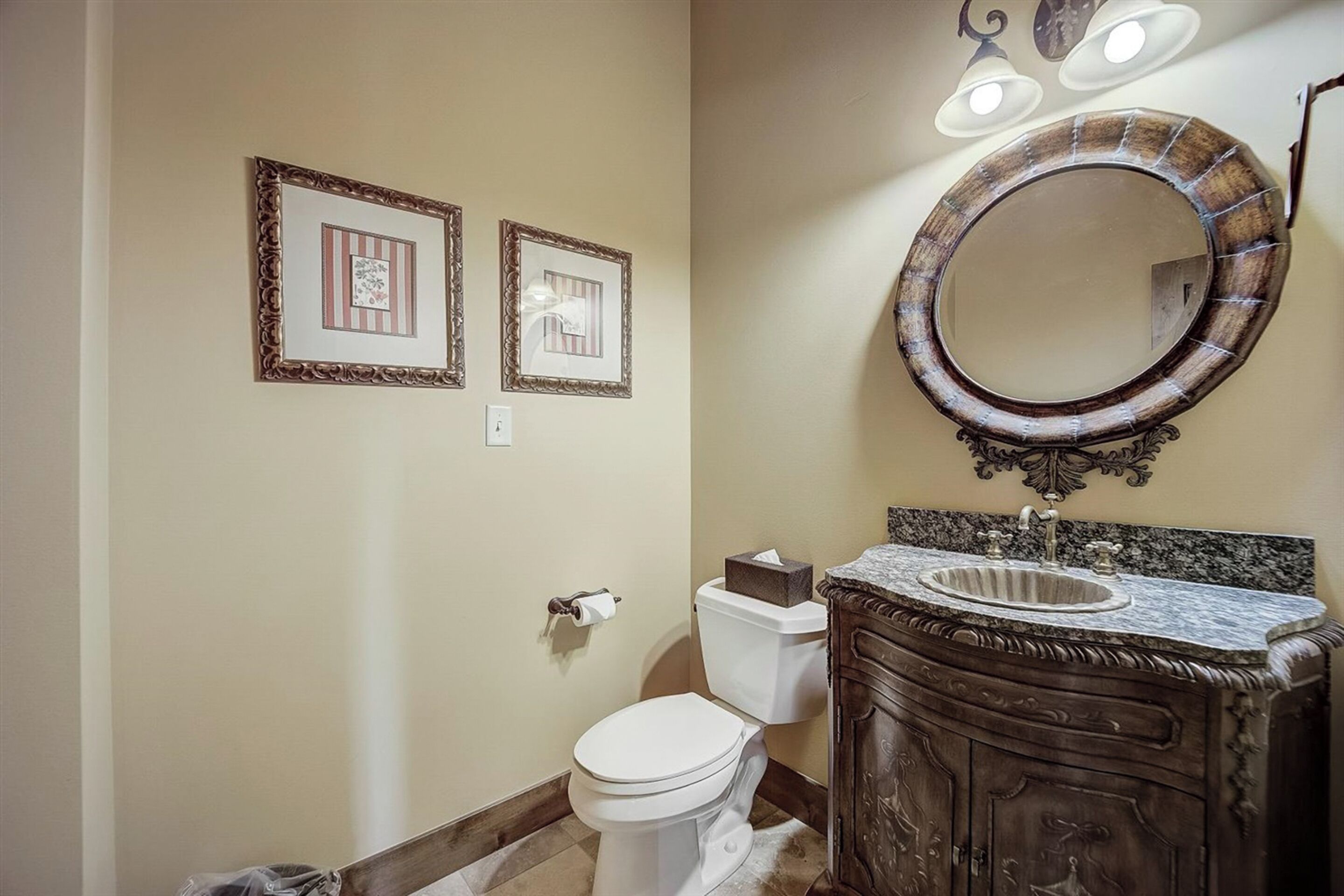 Une salle de bain comprenant des toilettes, un meuble-lavabo avec un évier et un miroir. Des tableaux encadrés ornent le mur.