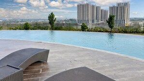 A swimming pool with lounge chairs, surrounded by a fence, with tall buildings in the background. - Newly 1BR Apt Cikarang with Pool Gym & Wi-Fi (Bekasi Regency)