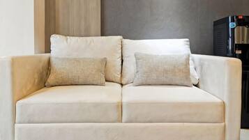 A beige sofa with two pillows against a wall with a vertical wooden panel and a black object to the right.