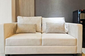 Un sofá color beige con dos almohadones frente a una pared con paneles de madera verticales y un objeto negro a la derecha.
