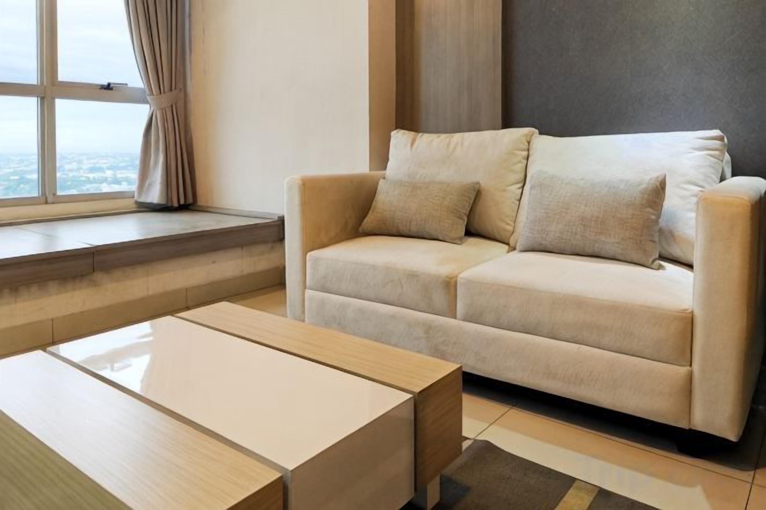 Un soggiorno moderno con un divano color beige, un tavolino in legno e un'ampia finestra con tende.