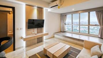 A modern living room with a flat-screen TV, a sofa, a coffee table, and a large window with a city view.