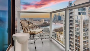 En balkon med udsigt over byens skyline, en fletstol og et lille bord.