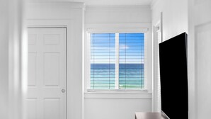 A room with a door, a window with a view of the ocean, and a flat-screen TV.