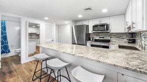 A modern kitchen with white cabinets, granite countertops, stainless steel appliances, and a breakfast bar with stools.