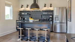 A modern kitchen with a central island, bar stools, a stainless steel refrigerator, and a pendant light. - Deluxe Four-Bedroom Suite + Balcony | The Carter (Nashville)