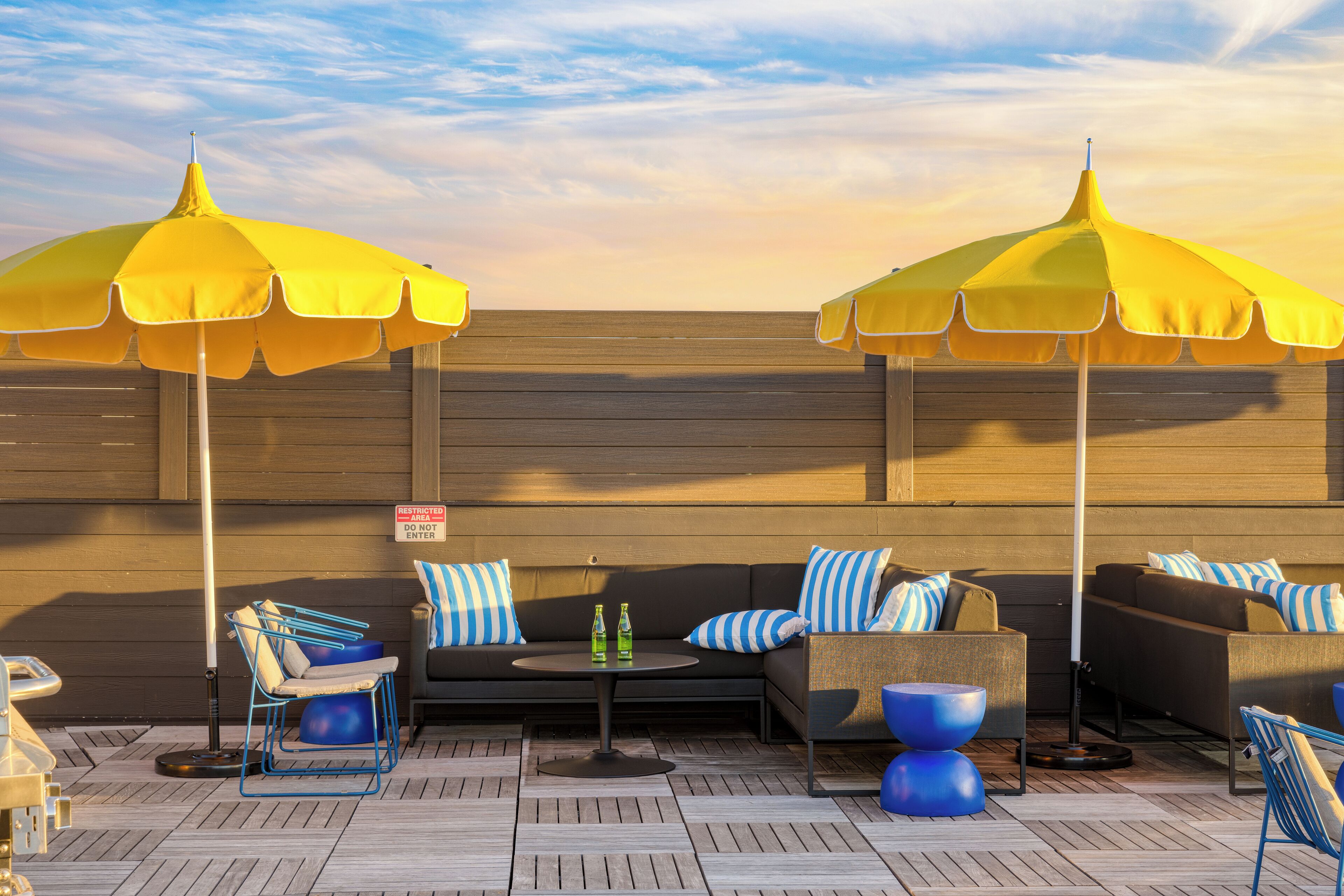 Un espace de détente aménagé sur le toit, avec des parasols jaunes, un ensemble de canapés et une petite table sur laquelle sont posées des bouteilles.