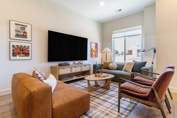 Una sala de estar moderna con un sofá, un sillón y una mesa de centro, un televisor de pantalla plana y cuadros enmarcados en la pared.