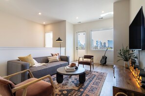 A modern living room with a sofa, armchairs, a coffee table, and a city view through large windows.