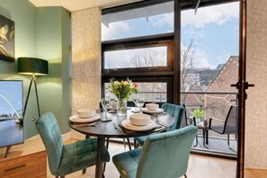 A dining area with a round table, four chairs, a vase with flowers, and a view of the outside through large windows. - Friarsgate Apartment by Week2Week (Newcastle)