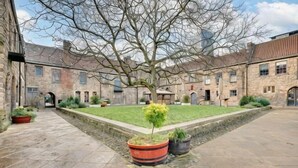 A courtyard with stone pathways, a central lawn, and a large tree. - Friarsgate Apartment by Week2Week (Newcastle)
