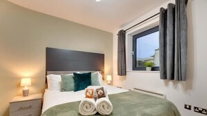 A neatly arranged bedroom with a bed, pillows, a window, and a nightstand with a lamp. - Friarsgate Apartment by Week2Week (Newcastle)