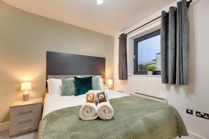 A neatly arranged bedroom with a bed, pillows, a window, and a nightstand with a lamp. - Friarsgate Apartment by Week2Week (Newcastle)