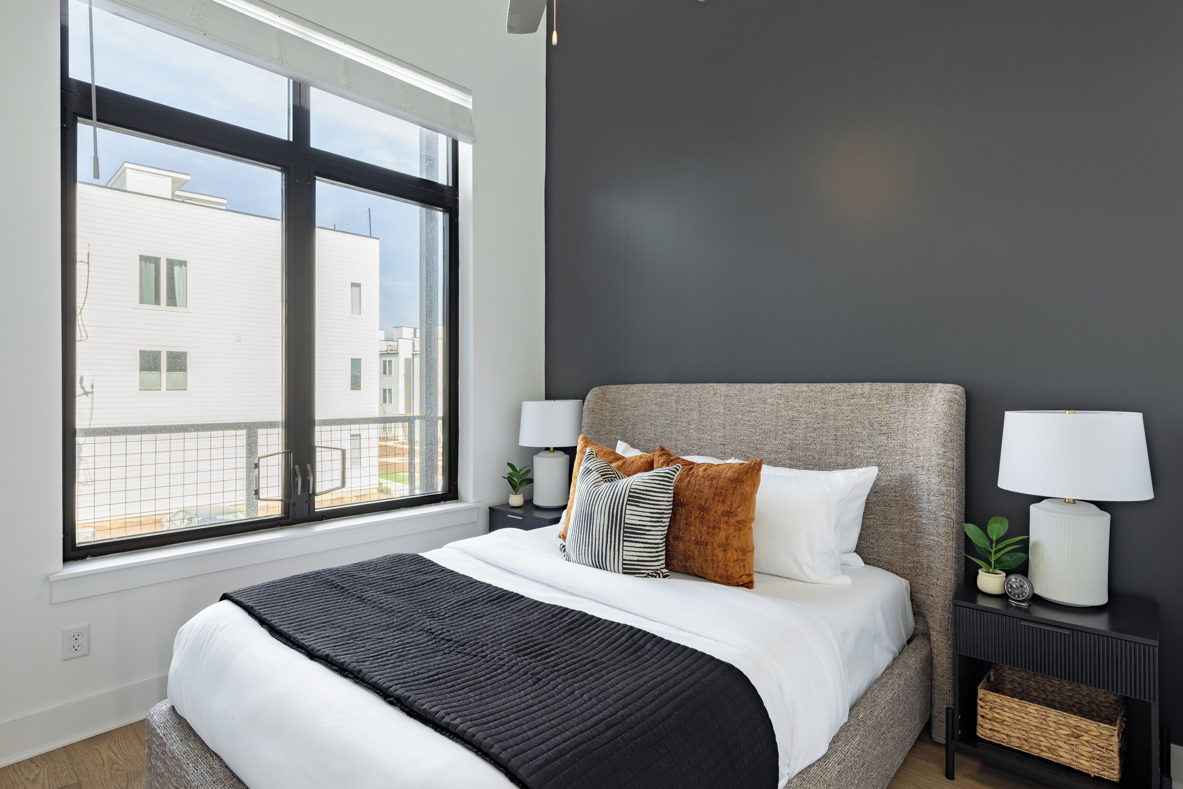 Une chambre moderne avec un grand lit, une table de chevet avec une lampe et une vue sur les bâtiments à travers la fenêtre.