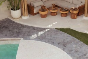 A pool area with a curved edge, a seating area with a sofa and wooden stools, and a potted plant. - Plawa Laguna (Bali)