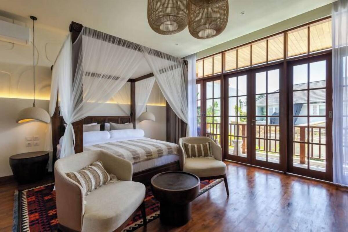 Un dormitorio amplio con una cama grande, una zona de estar con sillas, una mesita redonda y ventanas grandes que ofrecen vistas al exterior.