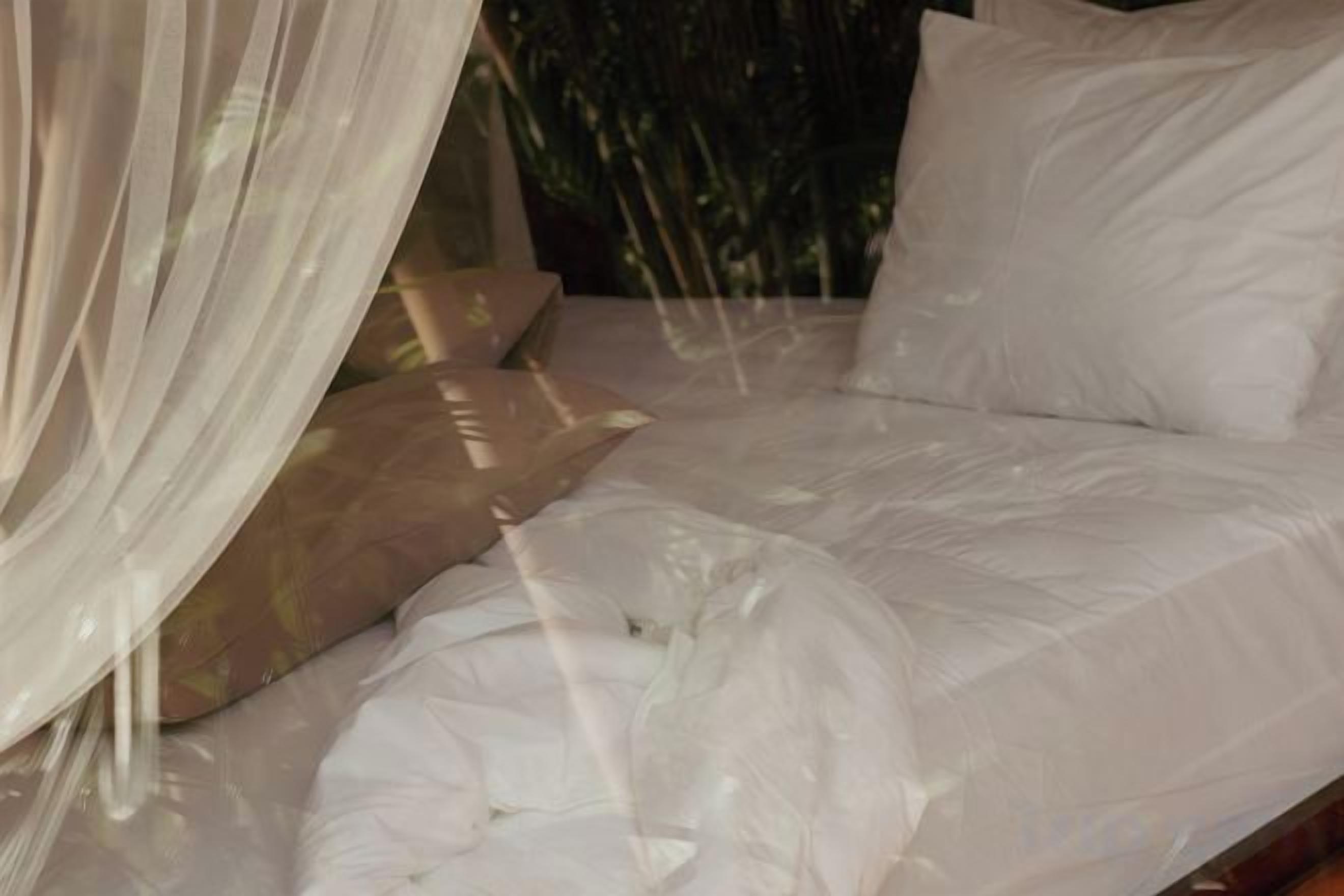 Una cama con ropa de cama blanca y un dosel ligero.