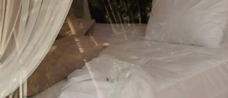 Una cama con ropa de cama blanca y un dosel ligero.