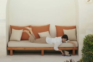 A person lying on a sofa with a book, in a room with a plain wall and a small plant. - Plawa Laguna (Bali)