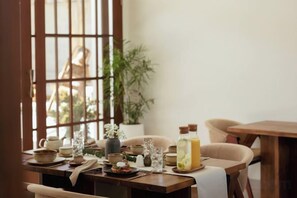 A dining table set with various dishes, glasses, and a bottle of water, with a view of a building through a window. - Plawa Laguna (Bali)