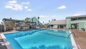 En klarblå pool med solstolar och en möblerad sittgrupp under tak.