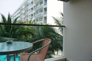 Un balcón con una mesa redonda y una silla de mimbre, con vistas a una piscina y un edificio con balcones.