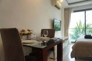 Une chambre d’hôtel avec une table à manger dressée pour deux personnes, un lit recouvert d’une courtepointe beige et une fenêtre donnant sur un paysage verdoyant.