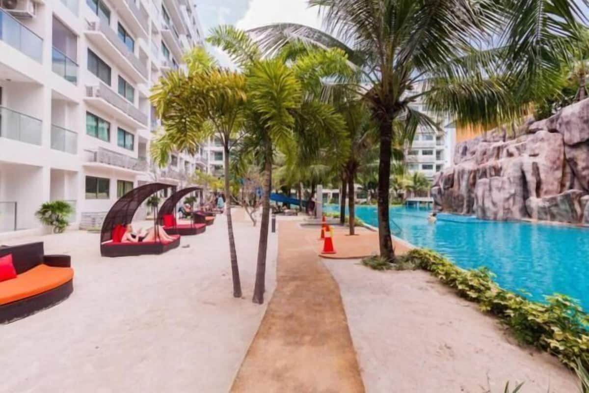 A hotel pool area with a concrete pathway, palm trees, and a rock formation.