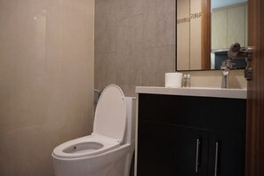 Une salle de bain comprenant des toilettes, un lavabo, un miroir et un meuble de rangement.