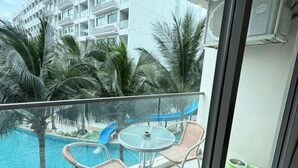 Un balcon avec une piscine, des chaises et une vue sur un immeuble bordé de palmiers.