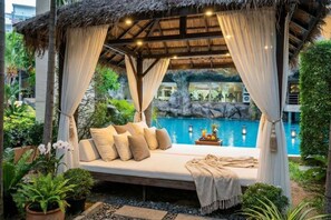 Un espace extérieur accueillant, avec un banc rembourré, entouré d’une végétation luxuriante et d’une piscine.