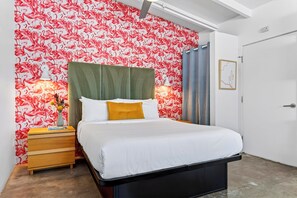 A bedroom with a bed, a nightstand, a lamp, a vase with flowers, and a wall with a flamingo pattern.