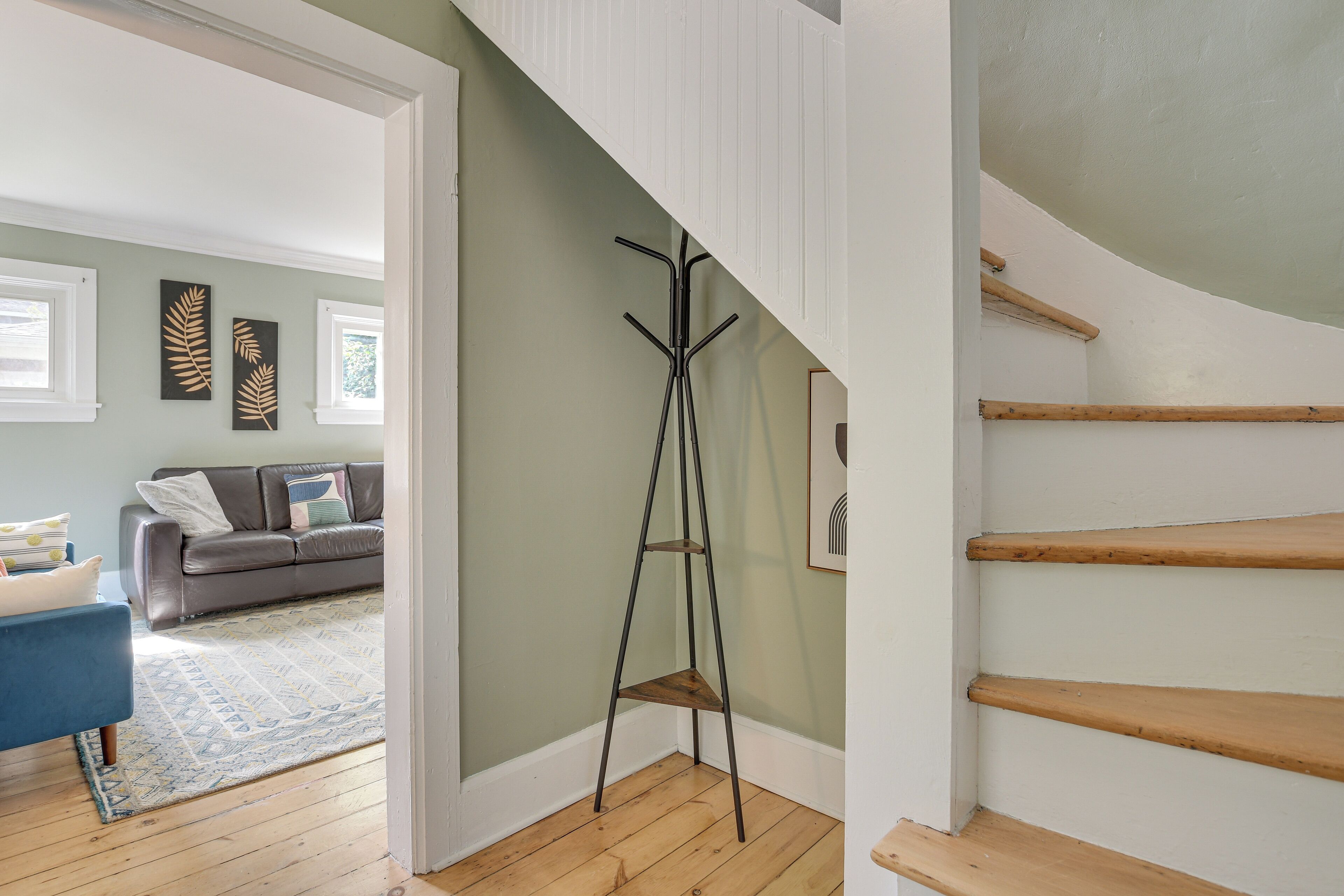 A staircase with wooden steps and a metal coat rack in a room with a grey couch, a patterned rug, and wall art.