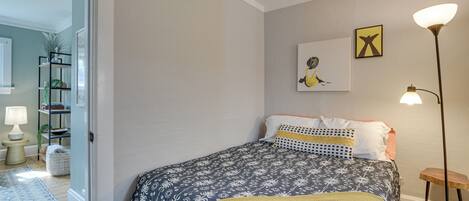 Ein Schlafzimmer mit einem Bett, einer Nachttischlampe, einer Stehlampe und einer Wand mit einem gerahmten Bild.