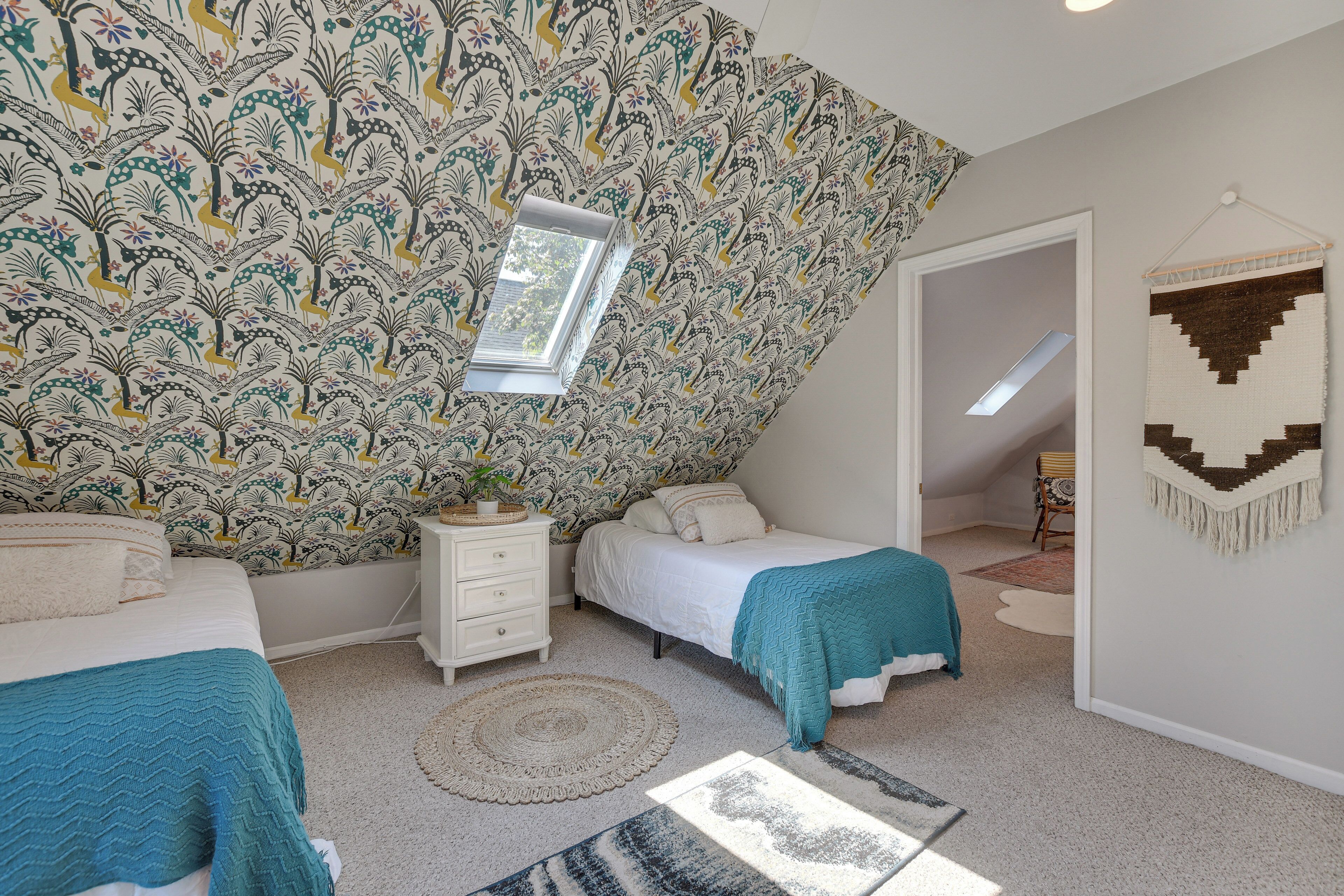 Camera da letto con soffitto decorato, due letti, un comodino, una finestra e un arazzo appeso.