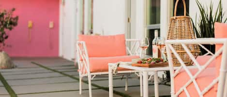 Un espace extérieur aménagé avec des meubles en osier blanc et des coussins orange, un panier en osier et une table sur laquelle se trouvent une bouteille et des verres.
