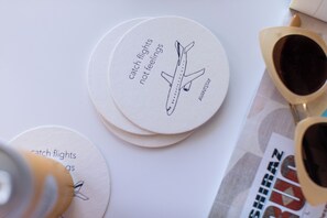 A stack of round coasters with airplane illustrations and text, a pair of sunglasses, and a small bottle. - Boutique Stay + Pool | 2BR Apartment at The Rosalie (Palm Springs)