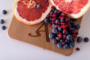 A wooden cutting board with a letter 'A' cutout, containing grapefruit halves, blueberries, and pomegranate seeds. - Boutique Stay + Pool | 2BR Apartment at The Rosalie (Palm Springs)