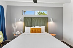 A modern hotel room with a large bed, two bedside lamps, a small table, and a window with a view of trees.