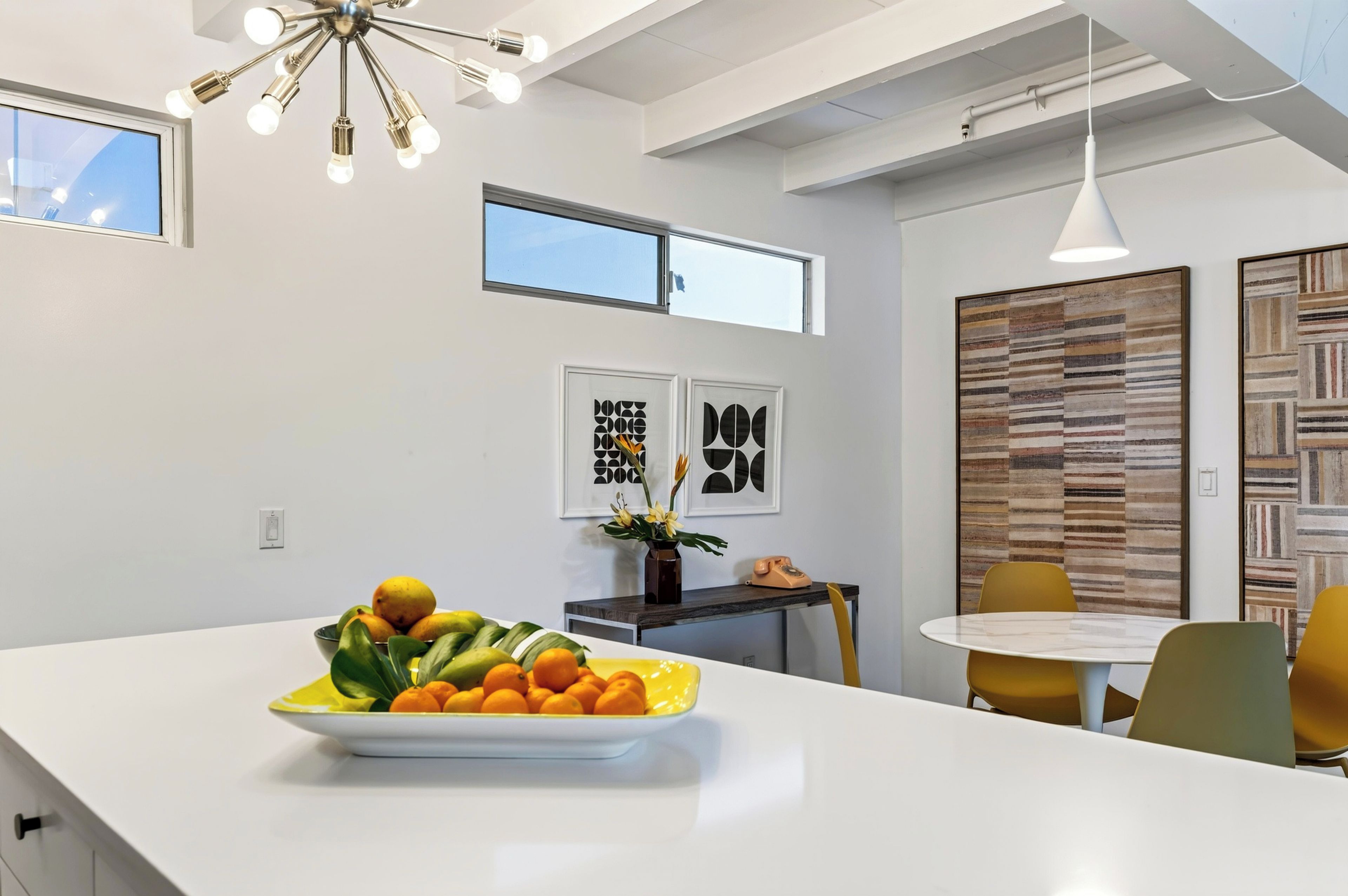 A modern kitchen with a central island, a dining area with yellow chairs, and artwork on the walls.