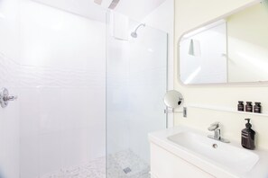 Ein modernes Badezimmer mit einer begehbaren Glasdusche, einem weißen Waschbecken und einem Spiegel darüber.