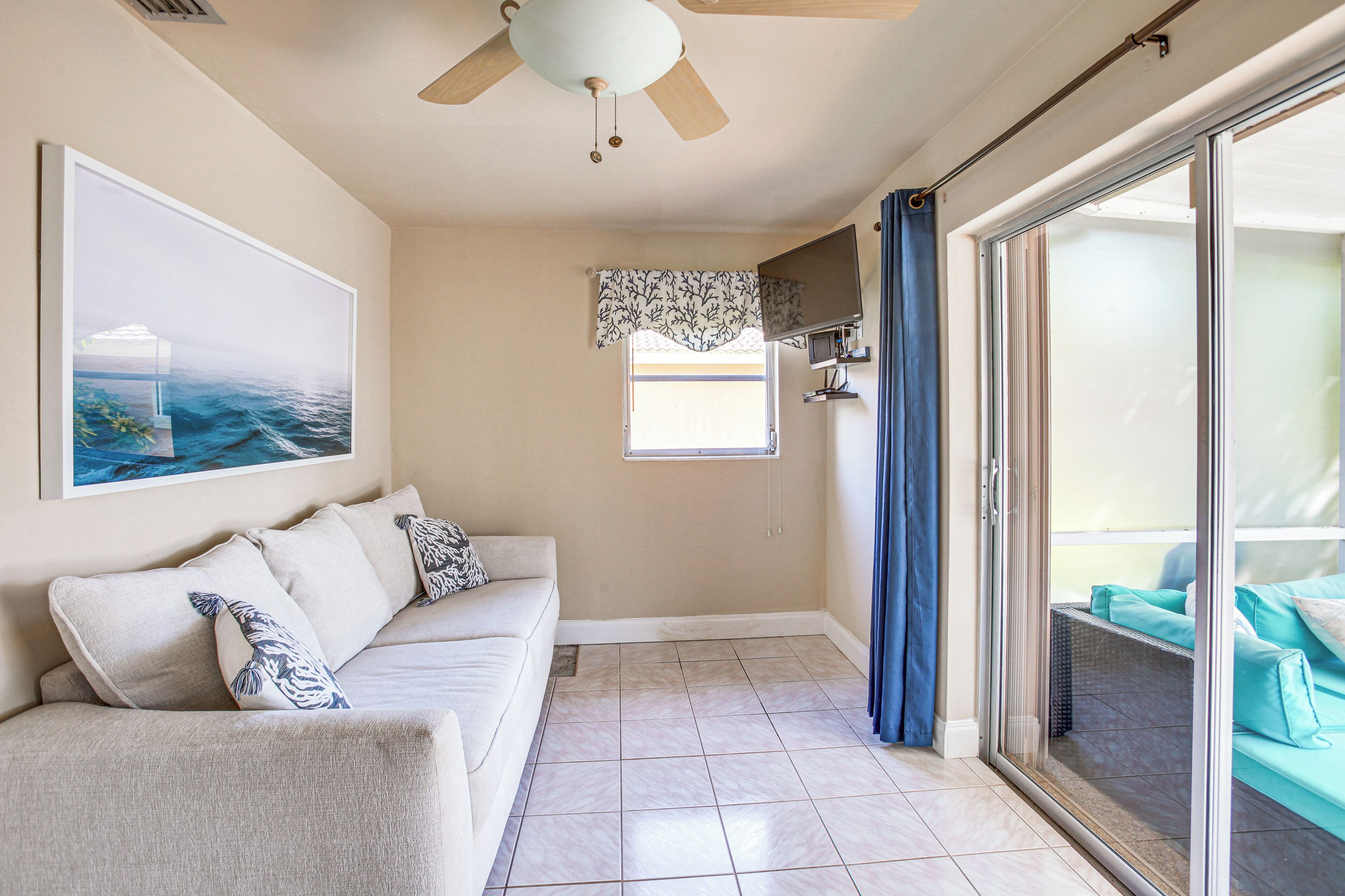 A living room with a beige sofa, a ceiling fan, a large framed picture, and a sliding glass door leading to an outdoor area.