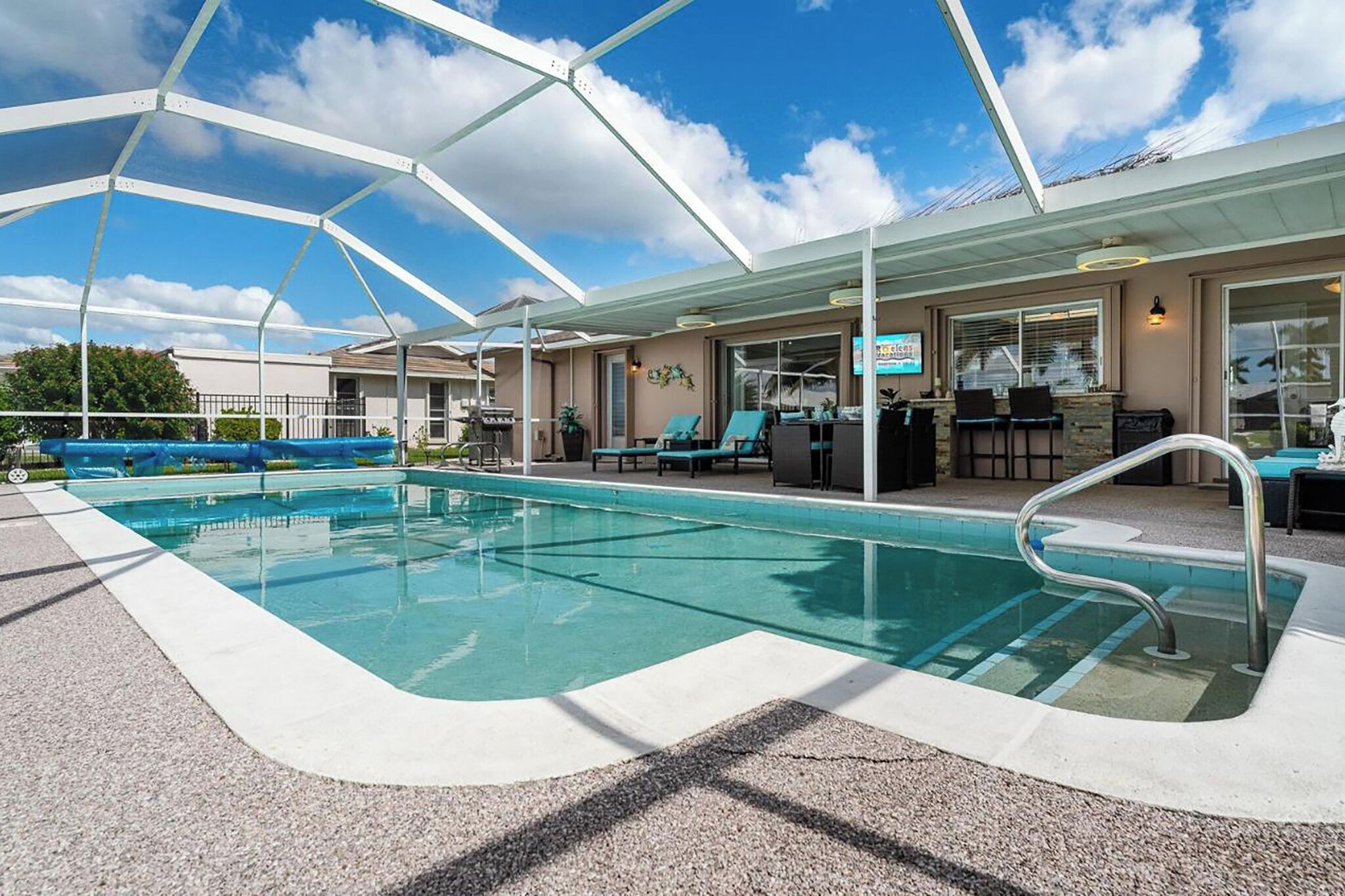 A pool area with a covered seating area, lounge chairs, and a bar.