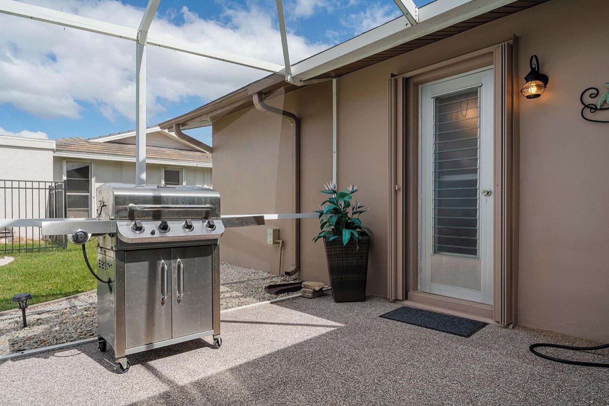 An outdoor grill area with a gas stove, a potted plant, and a door with a window.
