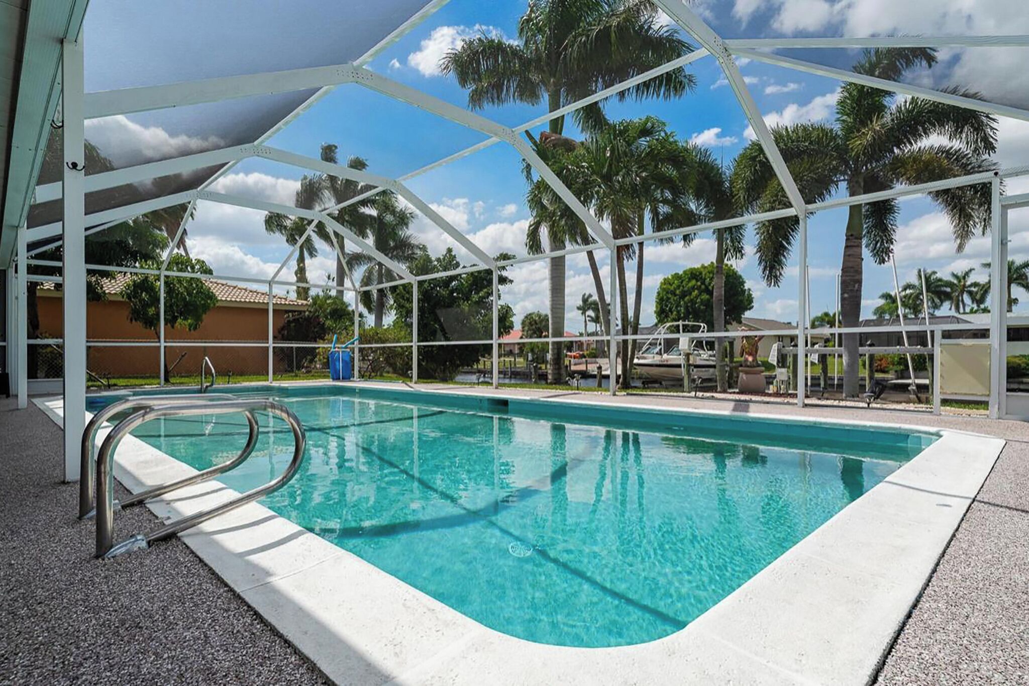 A swimming pool with a metal deck and palm trees in the background.