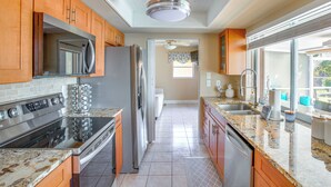 A modern kitchen with stainless steel appliances, wooden cabinets, granite countertops, and a view to the backyard. - Dock Your Boat: Waterfront Cape Coral Home w/ Pool (Cape Coral)